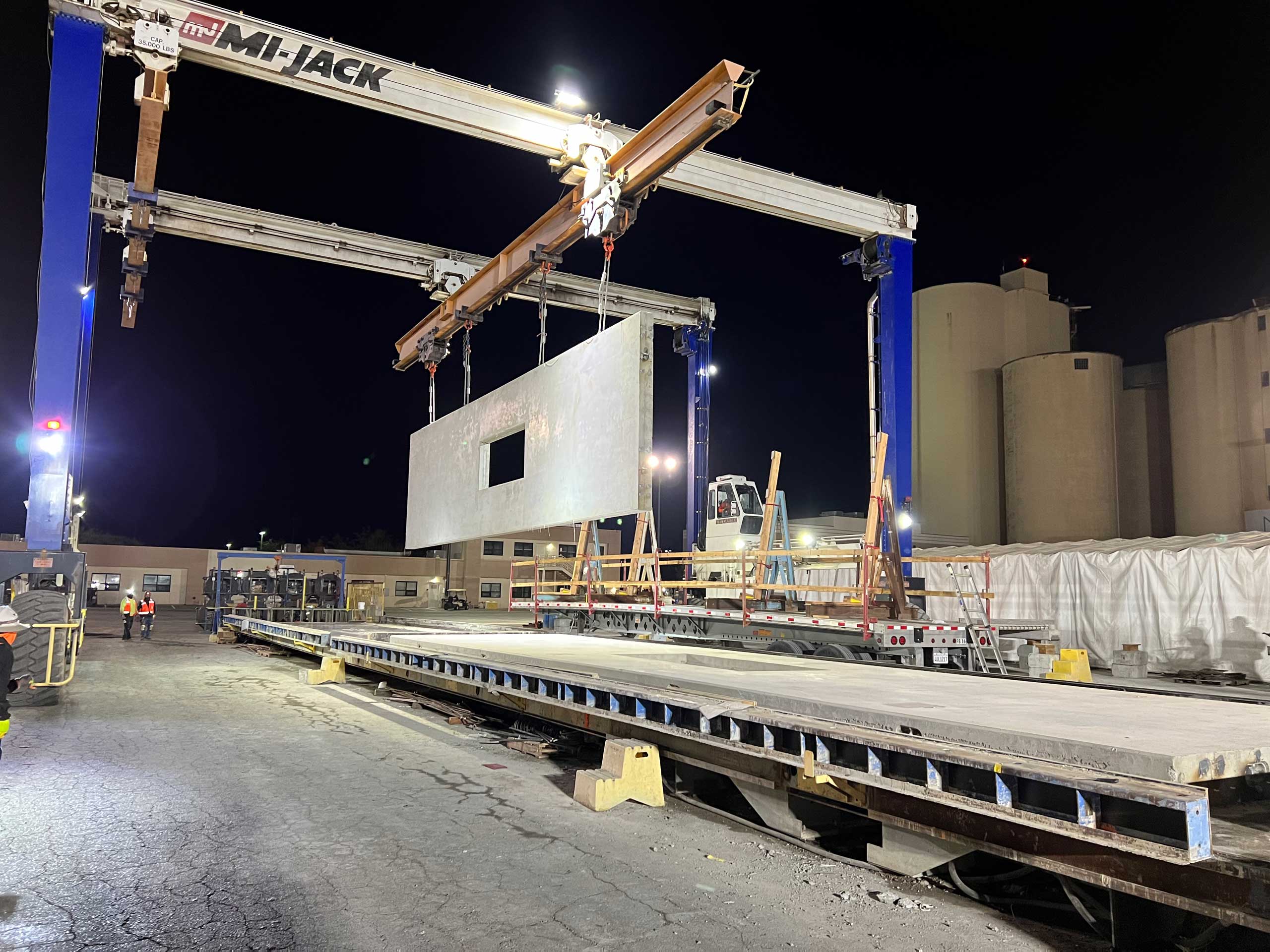 Crane lifting large concrete slab at night construction site.